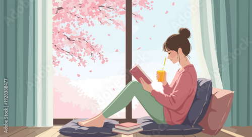 Young woman with hair bun sitting on floor cushions by window, reading a book and drinking orange juice, with pink cherry blossom trees visible outside