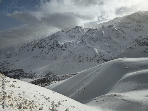 Photography Snow-covered mountain peaks under soft winter light, with drifting clouds enhancing the serene alpine landscape and untouched snowy slopes