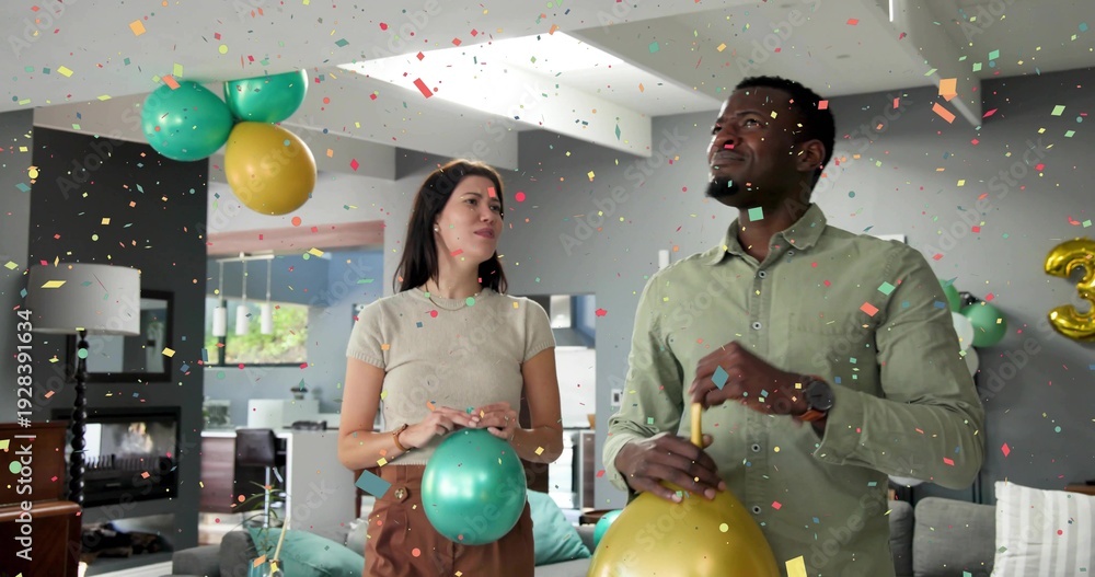 Naklejka premium Celebrating couple holding metallic balloons in living room, confetti falling, man in green shirt