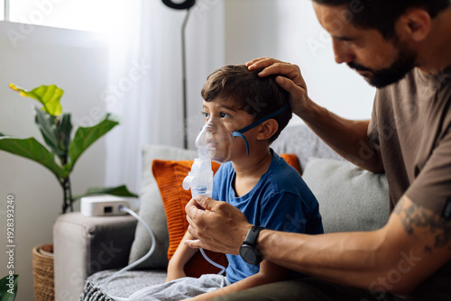 Father assisting young child during nebulizer therapy at home, showing parental care, pediatric respiratory treatment and emotional family support.