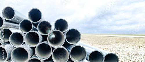 Slika na platnu At a construction site, water pipes are neatly stacked against the backdrop of an endless sky