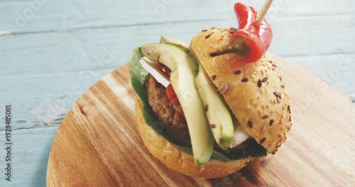 Resting seeded burger on blue table, showing avocado, greens, grilled patty, chili skewer