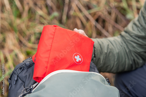 Person packing red first aid kit into backpack