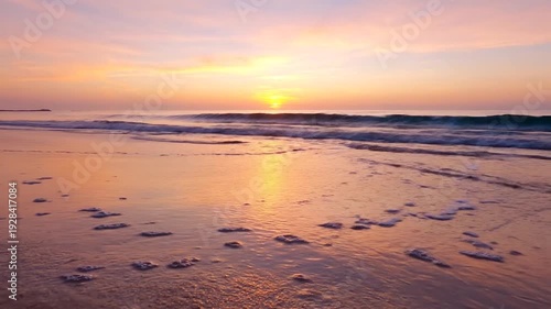 A sunrise over a calm ocean, with waves lapping the shore