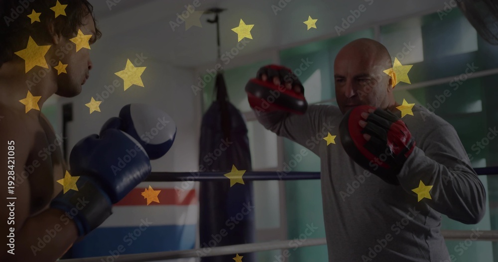 Obraz premium Coaching trainer holding red-black mitts in ring, boxer wearing blue gloves, gold stars, copy space