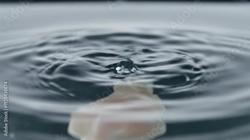 A clear water drop rests on a wet glass surface creating a gentle ripple and abstract blue reflection in this fresh macro shot