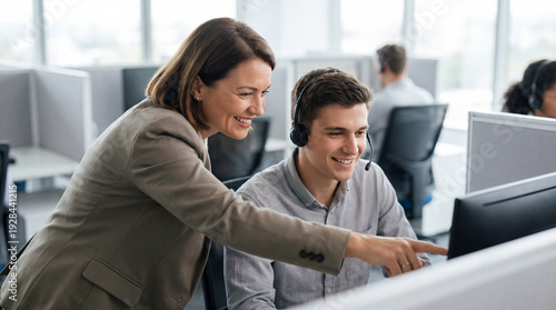 Manager coaches support agent at desk. Support team uses headset and monitor for customer support training, service quality focus for customer service week, back to work onboarding, new year goals