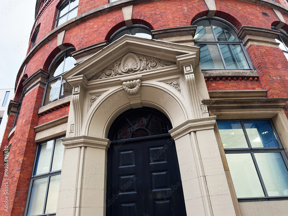 Obraz premium Elegant red brick building in Manchester UK with ornate archway entrance and black door front