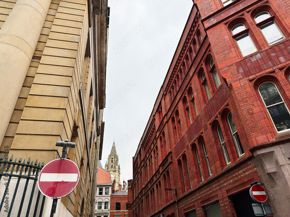 Obraz premium Historic urban street in Manchester with red brick buildings and a distant church spire