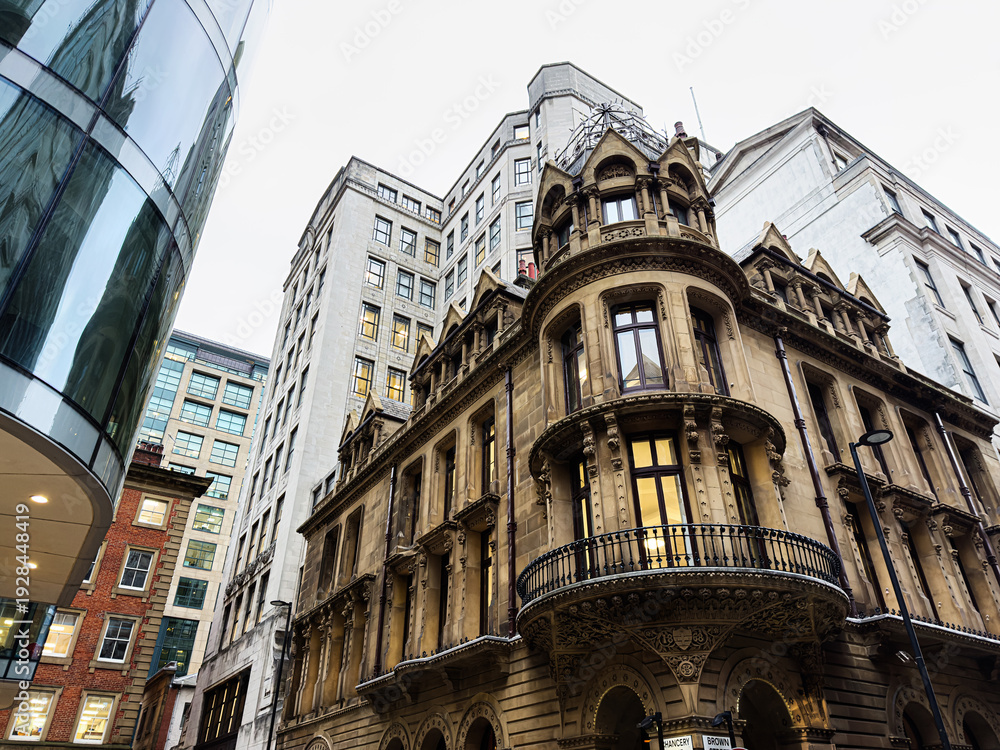 Obraz premium Historic sandstone Manchester building with ornate balcony amid modern urban buildings