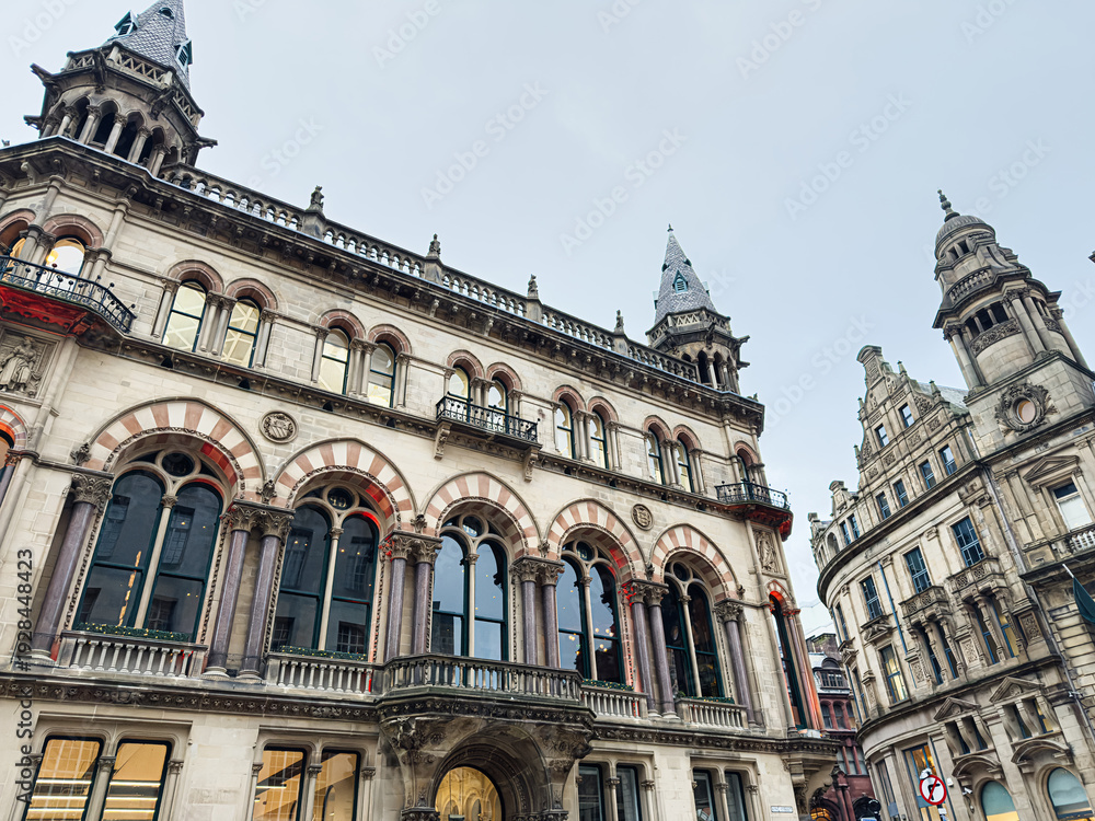 Naklejka premium Historic Manchester architecture with ornate arched windows and towers along a bustling street in city center
