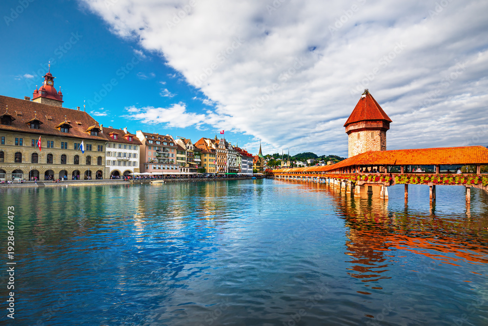 Obraz premium Beautiful view of Lucerne, Switzerland featuring the famous wooden Chapel Bridge with Water Tower over the Reuss River. Scenic cityscape with alpine mountains, clear water, and colorful historic archi