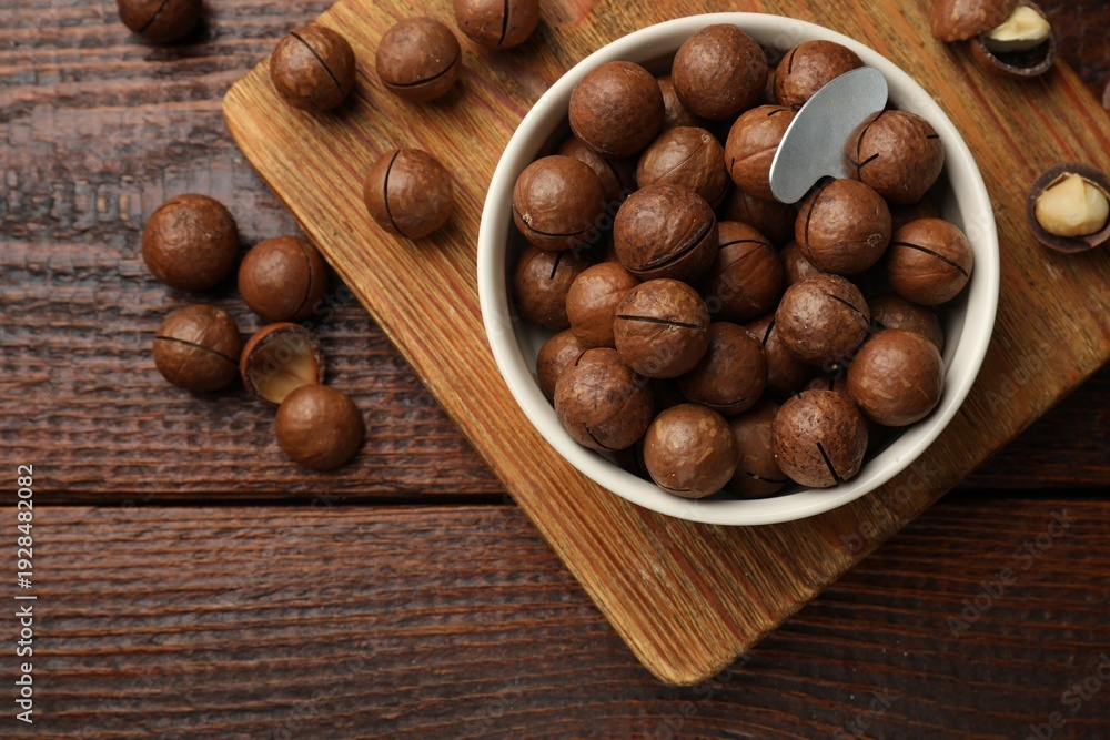 Obraz premium Macadamia nuts and metal key in bowl on wooden table, flat lay