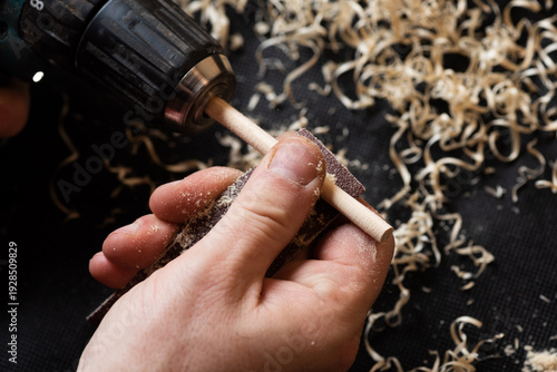 A craftsman sands a wooden part with sandpaper using a screwdriver