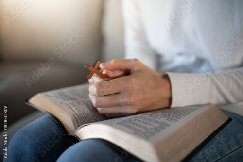 Fotografie Woman praying with open Bible cross in hand at home, faith and devotion concept