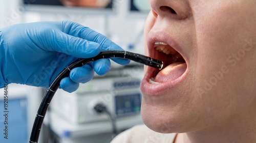 Flexible gastroscope inserted through mouth into esophagus with gloved hand in endoscopy suite