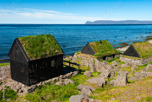Traditional turf houses at Ósvör maritime museum in Iceland, historic fishing huts with grass roofs overlooking the Atlantic Ocean on a sunny summer day.