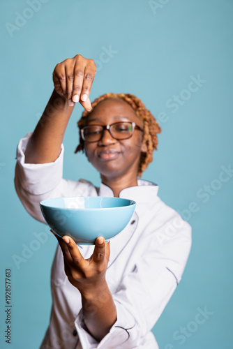 Obraz na plátne Happy woman chef seasoning cooked food in bowl, finishing dish with care