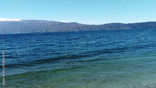Pebble beach in Toscolano Maderno with snowy mountains and Lake Garda, Italy