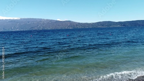 Pebble beach in Toscolano Maderno with snowy mountains and Lake Garda, Italy
