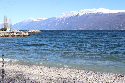 Pebble beach in Toscolano Maderno with snowy mountains and Lake Garda, Italy