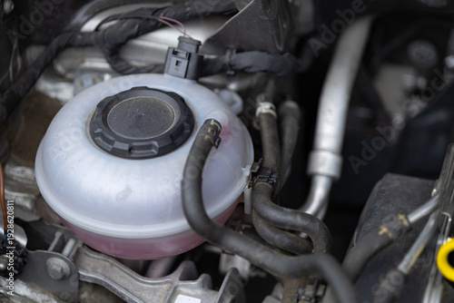 Detailed view of a car coolant expansion tank with pink antifreeze liquid under the hood of a modern vehicle. Automotive maintenance, engine cooling system and car service parts