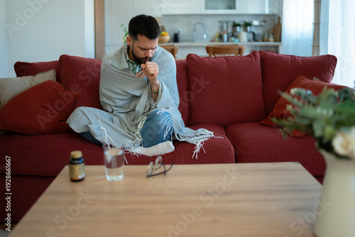 Sick man coughing on sofa feeling unwell at home