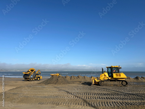 Diggers and dumpers levelling out the sand after a storm hit the beach