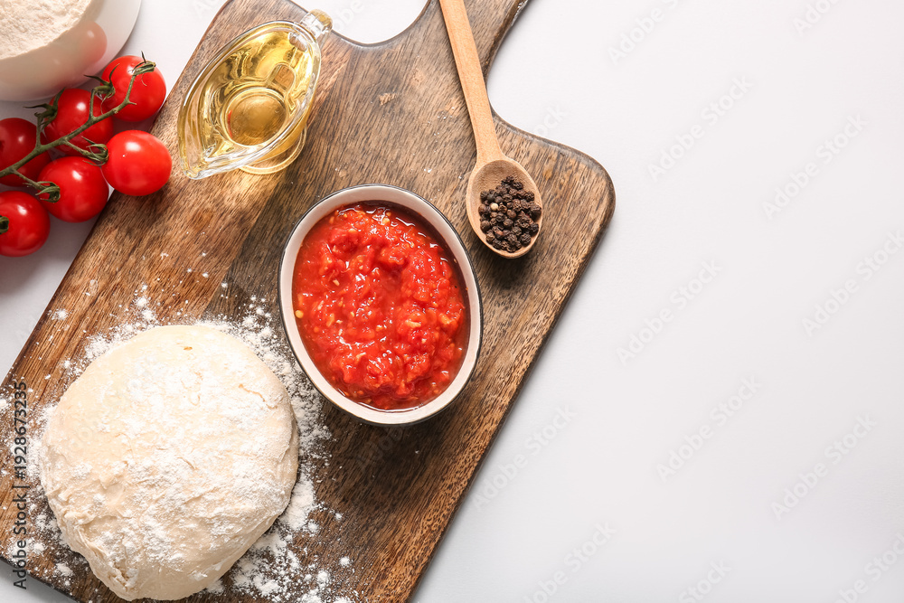 Fototapeta premium Board with raw dough, bowl of tasty tomato sauce and ingredients on white background
