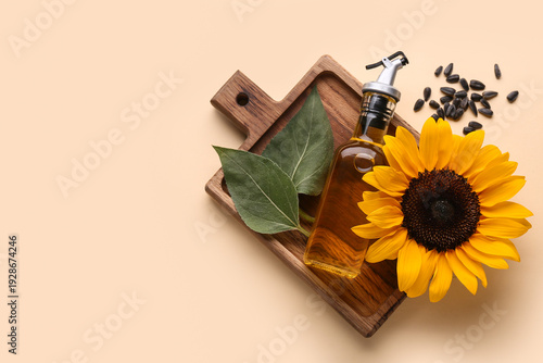Bottle of oil with sunflower, leaves and seeds on beige background