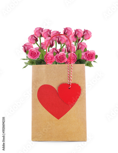 Pink roses in paper bag with red heart on white background. Romantic gift