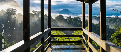 Panel kuchenny z motywem Breathtaking Panoramic View of a Misty Tropical Rainforest at Sunrise from a Wooden Balcony, Sunbeams Filtering Through Fog Over Lush Jungle Canopy and Distant Mountain Peak, Serene Nature Scene.