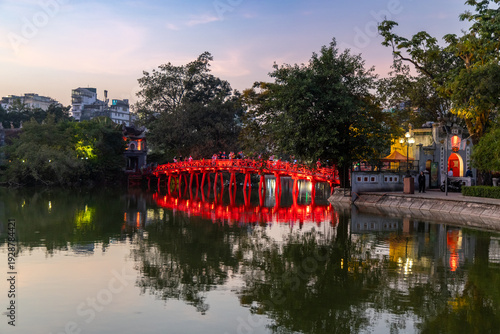 People visit the Huc Bridge at Hoan Kiem Lake in Hanoi, Vietnam, at dusk. The bridge connects to the Ngoc Son Temple, a popular tourist destination.