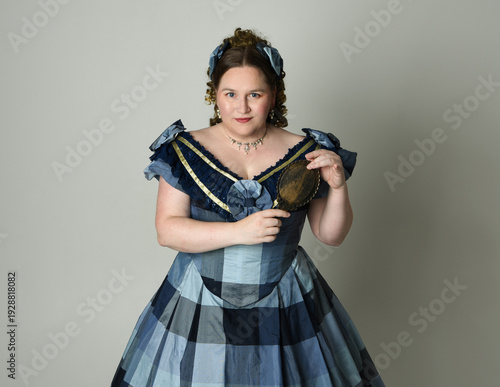 Fotografie portrait of Victorian Era Woman in historical victorian classical Blue Ball Gown costume, Plus Size Model, holding antique hand mirror