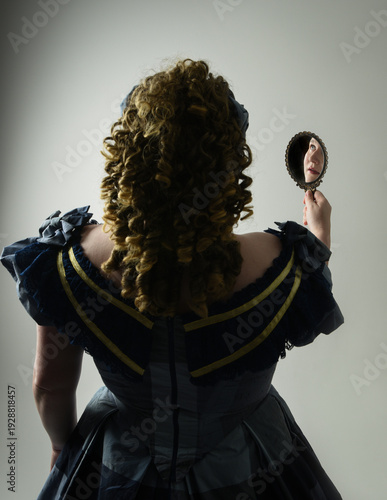 Fotografie portrait of Victorian Era Woman in historical victorian classical Blue Ball Gown costume, Plus Size Model, holding antique hand mirror