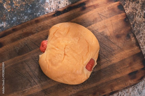 Close-up sausage bun placed on a wooden cutting board.
