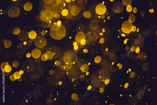 Defocused  golden bokeh lights in various sizes and colors on a dark background creating a dreamy and abstract visual effect