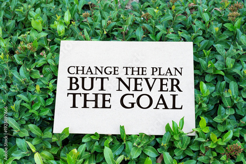 Fotografía A white card with the quote CHANGE THE PLAN BUT NEVER THE GOAL nestled in vibrant green leaves and foliage