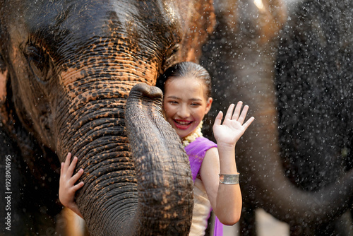 Fotografía Closeup Portrait of Beautiful Thai girl in the Thai traditional dress acting smile and waving hello with Asian elephant in the Thailand Songkran water festival outdoors