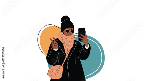 Fashionable young woman in a warm winter coat, scarf, and hat takes a selfie with her smartphone while making a peace sign gesture.