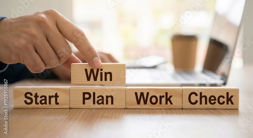 Blocks are stacked on a wooden table with words showing steps to success and a laptop in the background during a work session