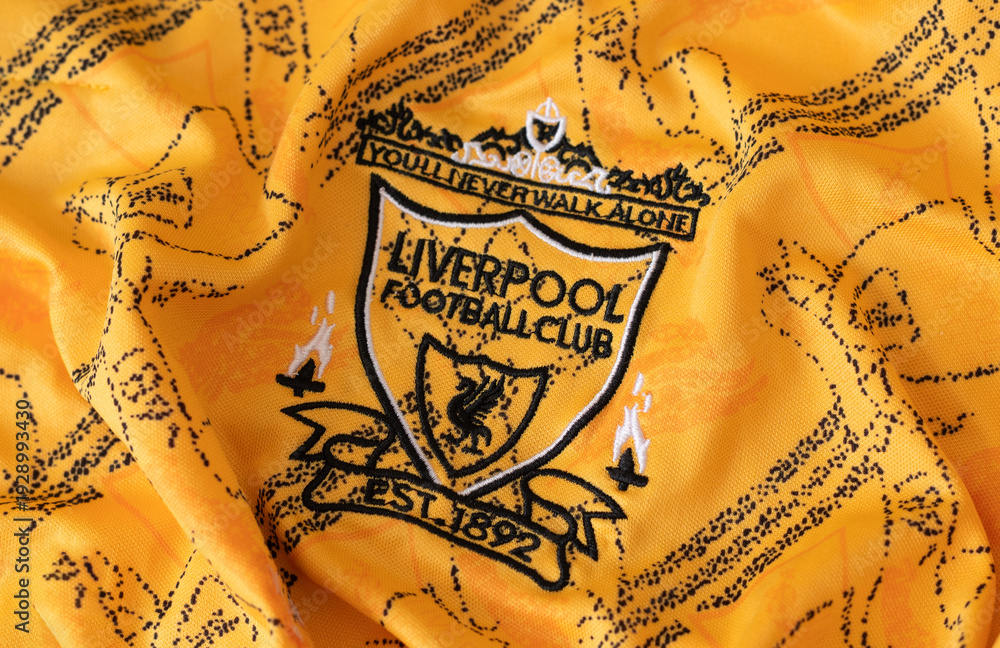Fototapeta premium Kyiv, Ukraine. February, 2026. Close-up of the Liverpool Football vintage club crest embroidered on a yellow textured sports jersey fabric. retro logo