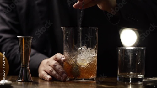 Bartender preparing an old fashioned cocktail in a mixing glass.