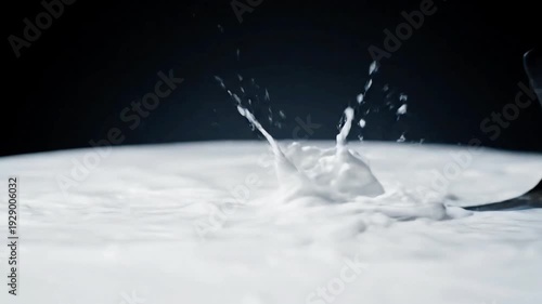 A dynamic close-up shot of a white liquid splashing upwards, likely milk or cream, with droplets frozen in motion against a dark background.
