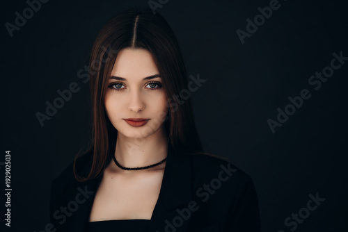 Portrait of a model, a beautiful brunette girl with straight long hair in a black jacket on a black background