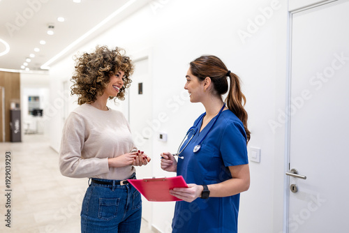 Photos Friendly nurse in blue scrubs consulting young patient in clinic hallway