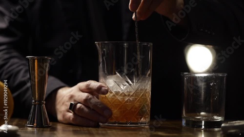 Bartender preparing an old fashioned cocktail in a mixing glass.