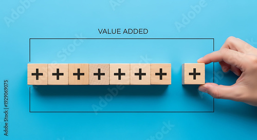 A hand adding value to a series of wooden blocks with plus signs on a blue background
