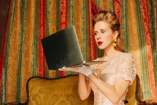Vintage styled woman in 18th century dress shocked using laptop indoors