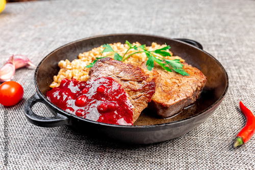 Close-up of a hearty hot dish - two pieces of fried meat (beef or pork) with loose spelt porridge, served in a traditional cast iron skillet.